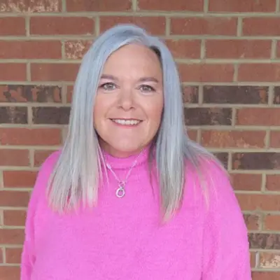 Woman with long hair, pink sweater, smiling.