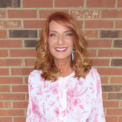 Smiling woman in floral blouse, brick background.