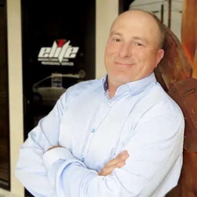 Man in blue shirt smiling, arms crossed.